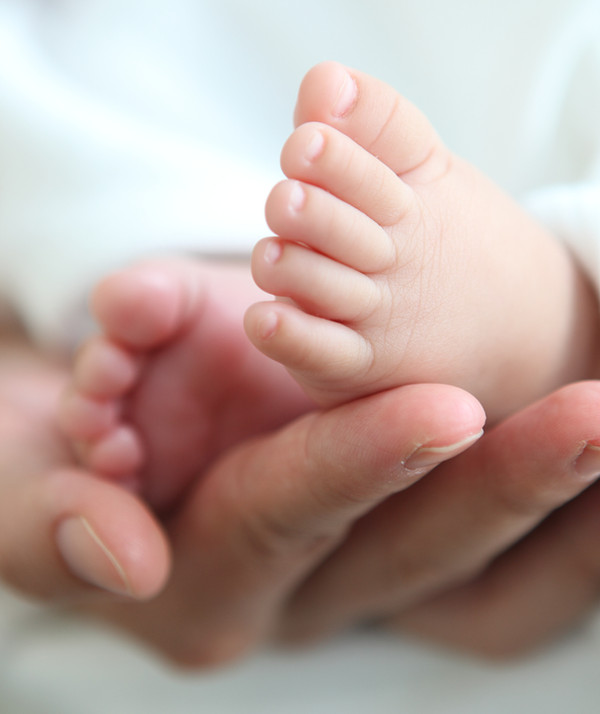 Tiny newborn baby feet cradled in loving hands